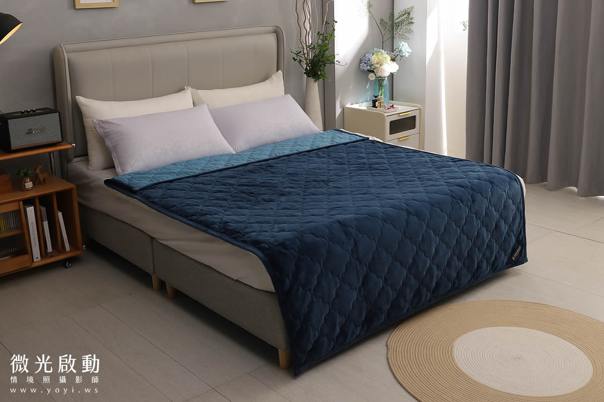 深藍色絎縫毛毯，搭配灰色與白色床單，突顯商品質感與色彩對比